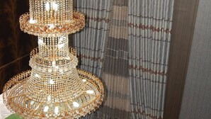 A multi-tiered chandelier with a decorative base, hanging in front of a curtain with a striped pattern. - Golden Valley Hotel Enugu (Nsukka)