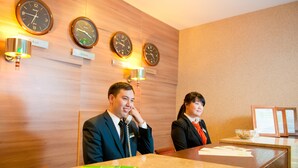 A hotel reception area with wooden paneling, clocks, and a reception desk.