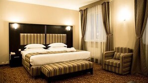 A hotel room with a large bed, a bedside table, a chair, and a window with curtains.