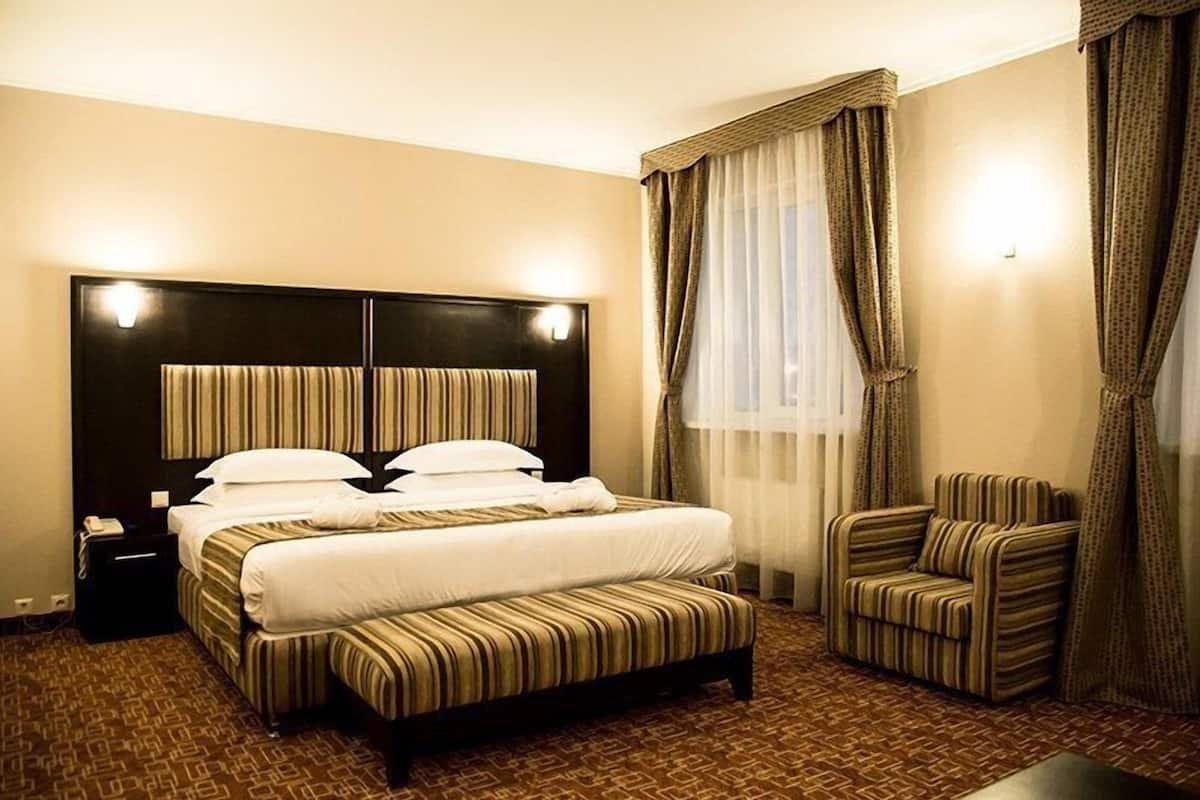 A hotel room with a large bed, a bedside table, a chair, and a window with curtains.