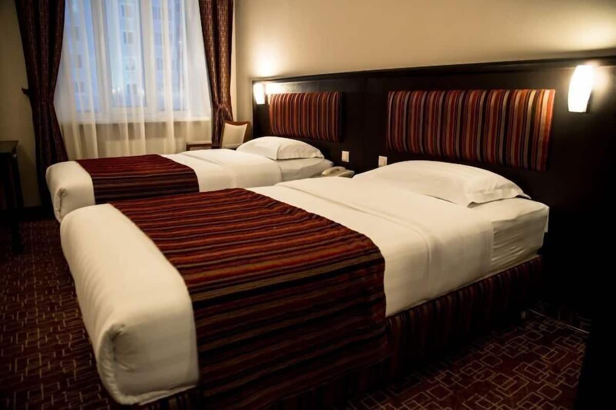 A hotel room with two beds, a large window with curtains, and a patterned carpet.