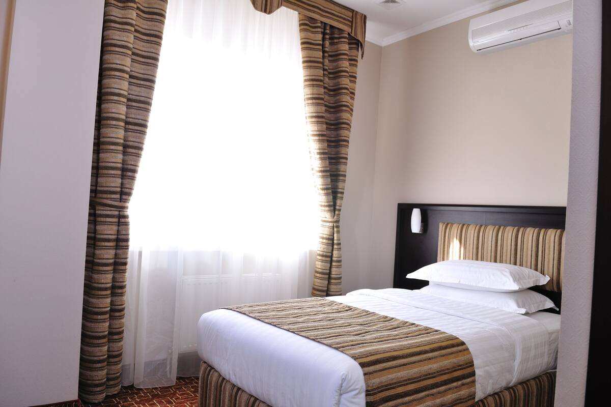A hotel room with a bed, curtains, and an air conditioning unit.