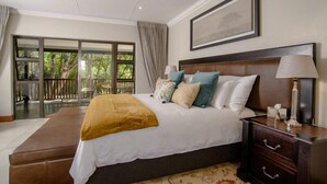 A bedroom with a large bed, a nightstand, and a window with a view of greenery. - The Reserve Boutique Hotel (Mbombela)