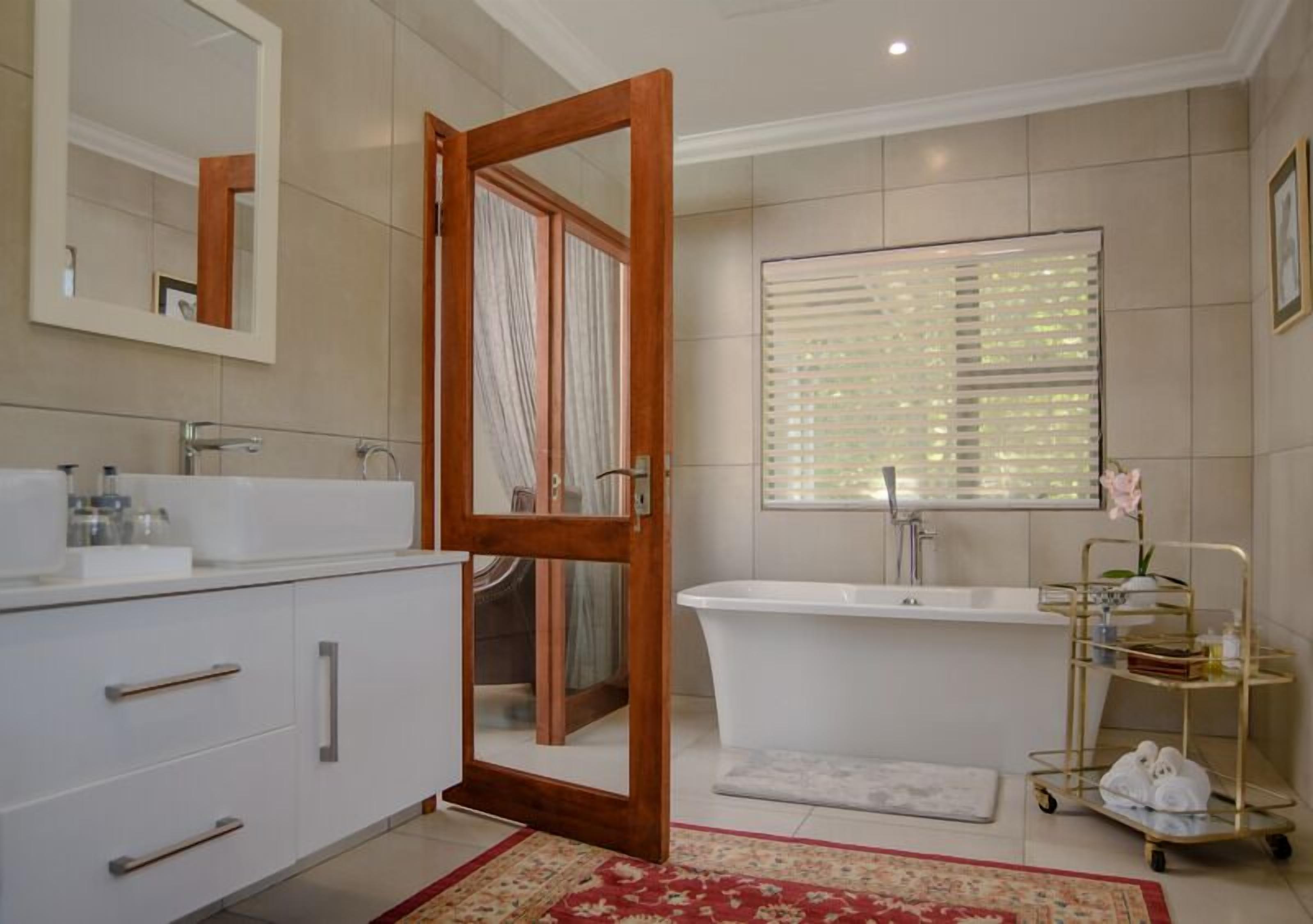 Ein Badezimmer mit einem weißen Waschbecken, einer Badewanne, einem Spiegel und einem Fenster mit Jalousien.