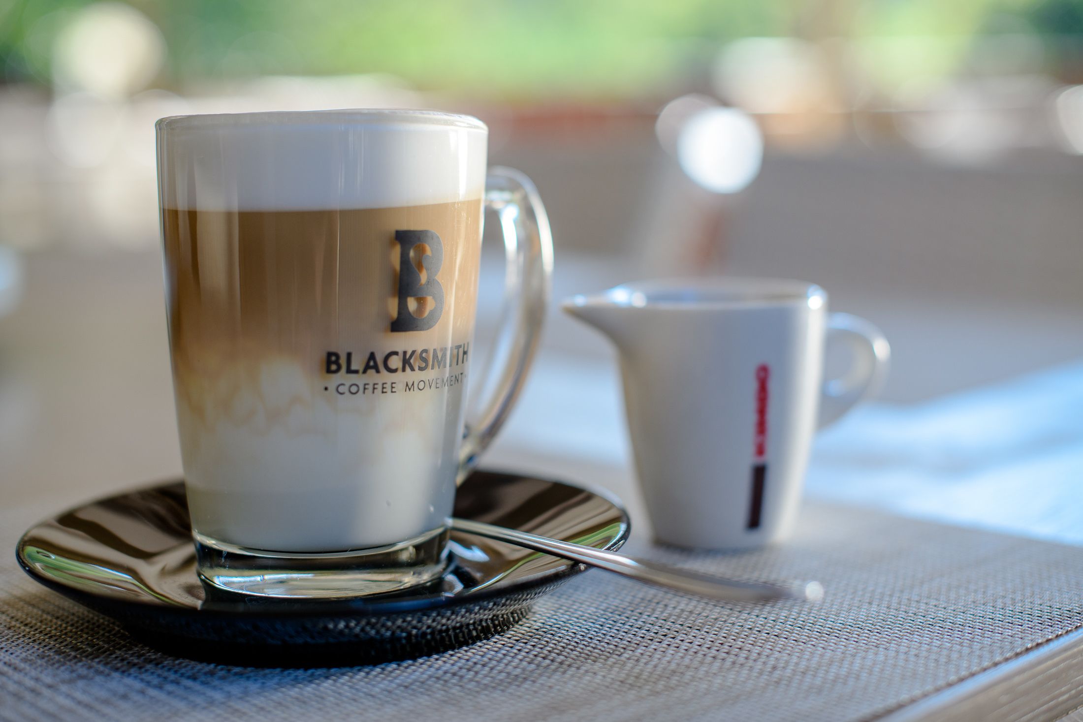 A coffee cup with a spoon on a saucer, a small pitcher, and a cup on a table.