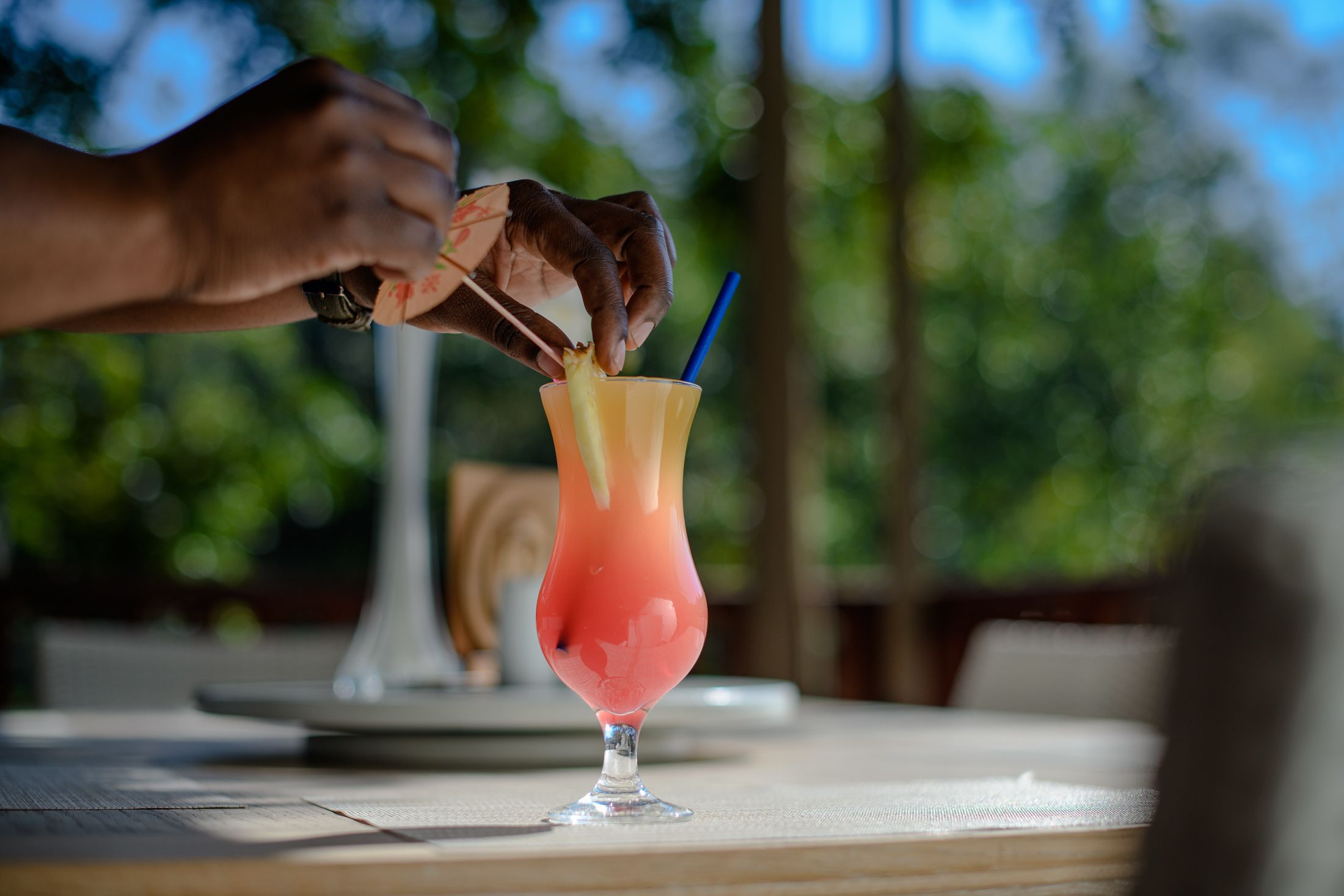 A hand placing a straw into a tall glass with a layered drink.