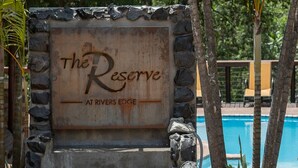 A sign for "The Reserve at Rivers Edge" with a pool and lounge chairs in the background. - The Reserve Boutique Hotel (Mbombela)