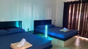 A hotel room with two beds, each with a blue bedspread and a white towel. There is a nightstand with a bottle and a remote control. - Coralview Beach Resort (Morong)