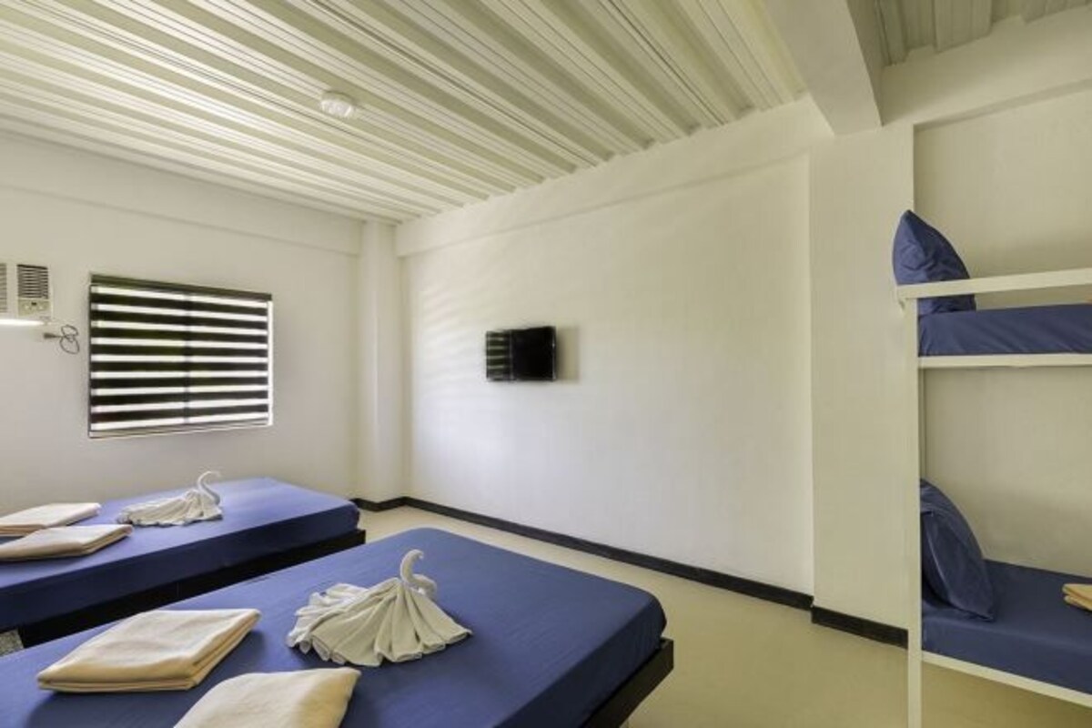 A room with bunk beds, a flat-screen TV mounted on the wall, and a window with blinds.