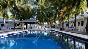 A swimming pool surrounded by palm trees and white buildings with outdoor seating. - Coralview Beach Resort (Morong)