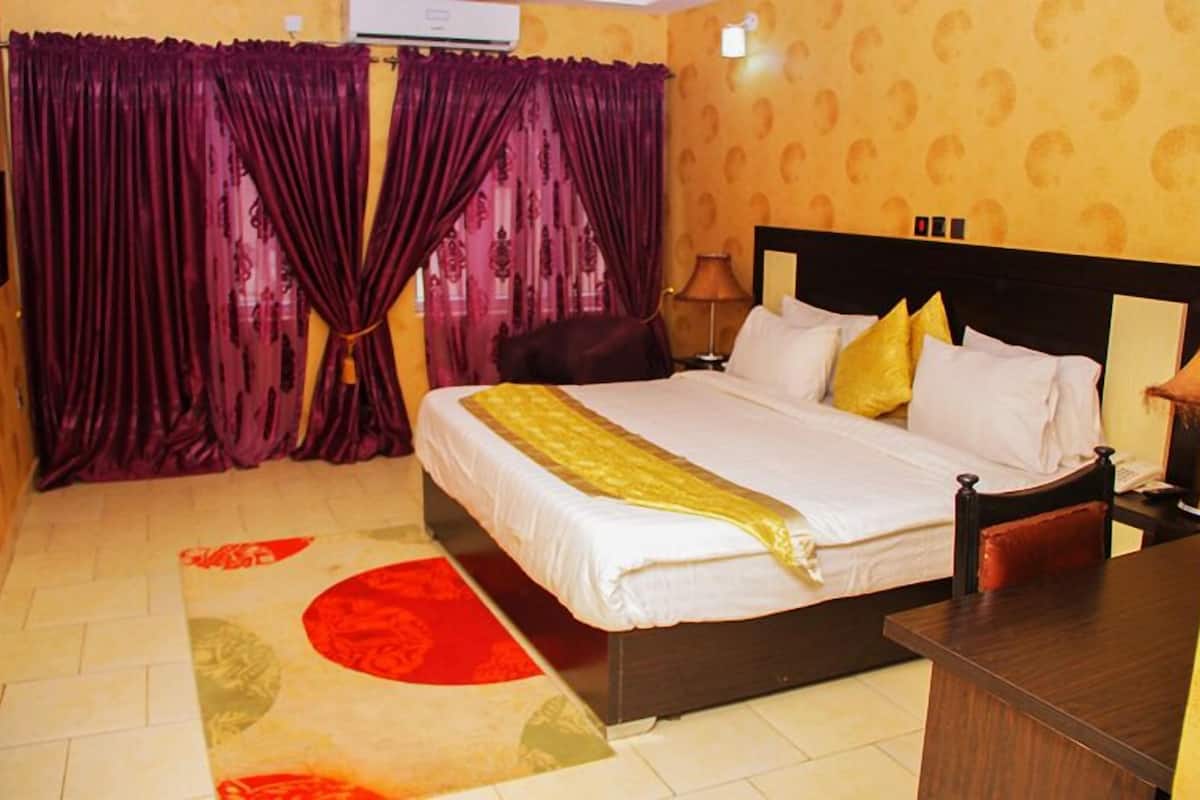 A hotel room with a bed, curtains, a nightstand, and a lamp.