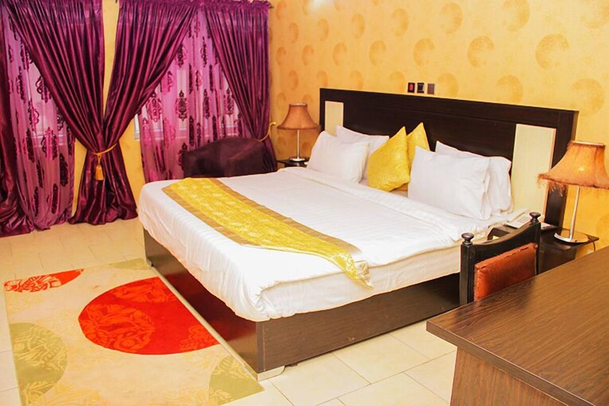 A hotel room with a bed, curtains, a nightstand, and a lamp.
