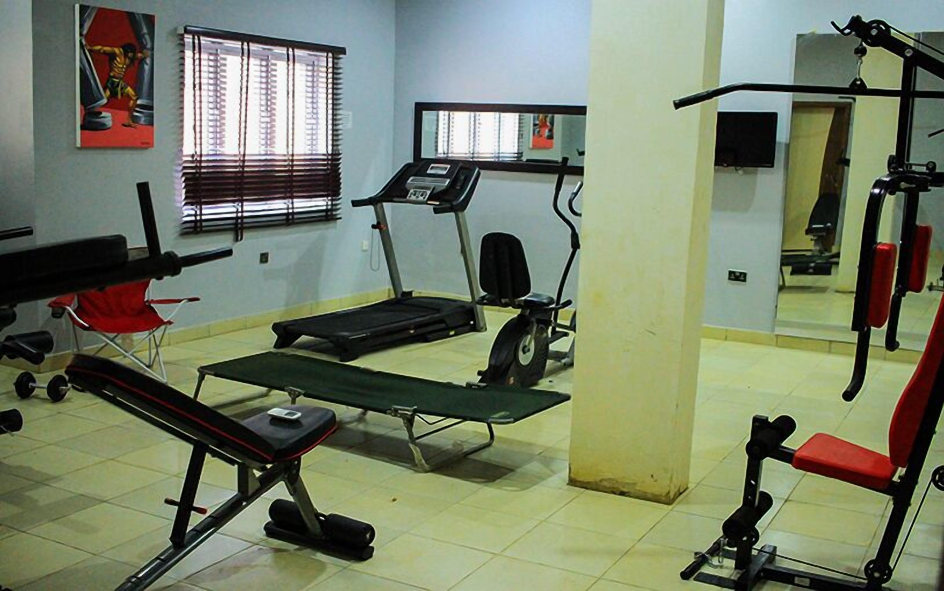 Ein Fitnessraum mit Trainingsgeräten, darunter Laufbänder, eine Hantelbank und ein Squat-Gestell.