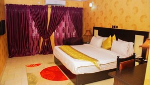 A hotel room with a bed, curtains, a nightstand, and a lamp. - Psalm Hotel (Enugu)