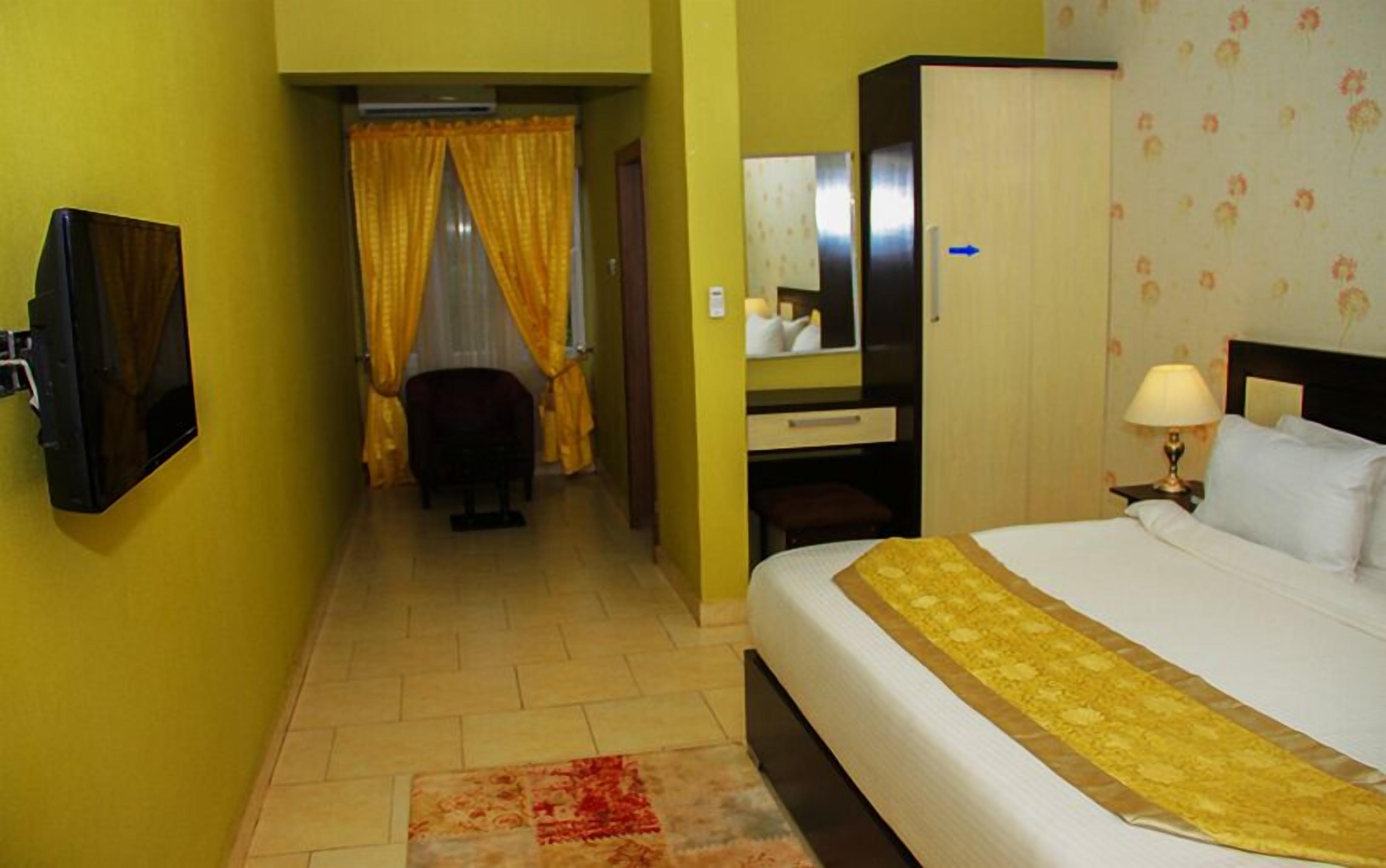 Habitación de hotel con cama, escritorio, silla, televisor y baño con cortinas amarillas.
