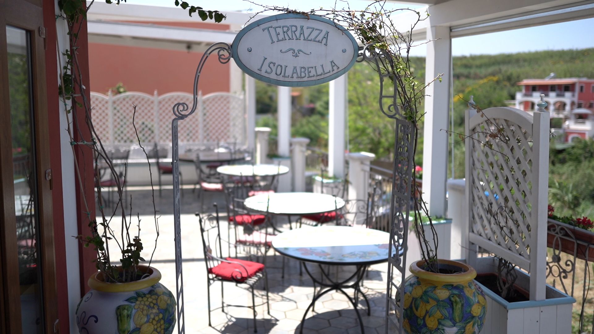 An outdoor seating area with round tables and chairs, a sign reading "TERRAZZA ISOLABELLA", and potted plants.