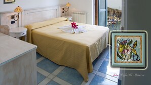 Habitación de hotel con cama, una mesita, una silla, un radiador y una ventana con contraventanas.