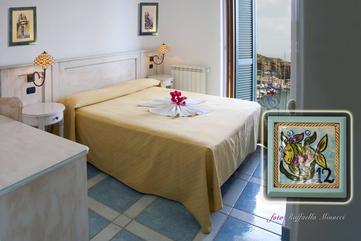 Une chambre d’hôtel avec un lit, une petite table, une chaise, un radiateur et une fenêtre avec des volets.