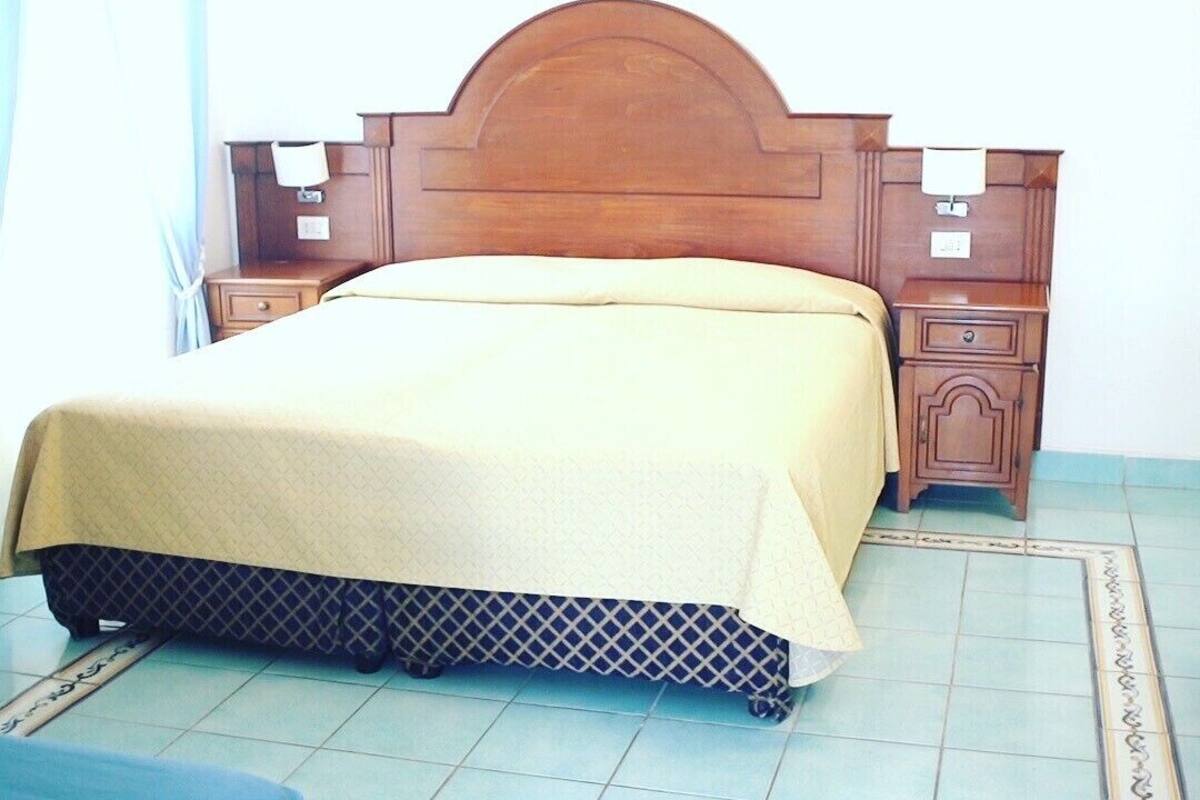 Une chambre à coucher avec une tête de lit en bois, un lit recouvert d’une couvre-lit à motifs, deux tables de chevet et une petite table de nuit.