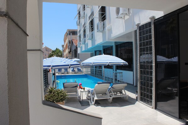 A pool area with lounge chairs and umbrellas, a small table, and a potted plant. - Tasan Apart Otel (Didim)