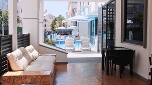 A hotel balcony with a pool, lounge chairs, and a dining table. - Tasan Apart Otel (Didim)