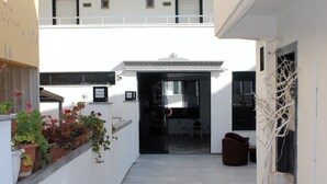 A narrow outdoor corridor with a white building, potted plants, and a brown chair. - Tasan Apart Otel (Didim)