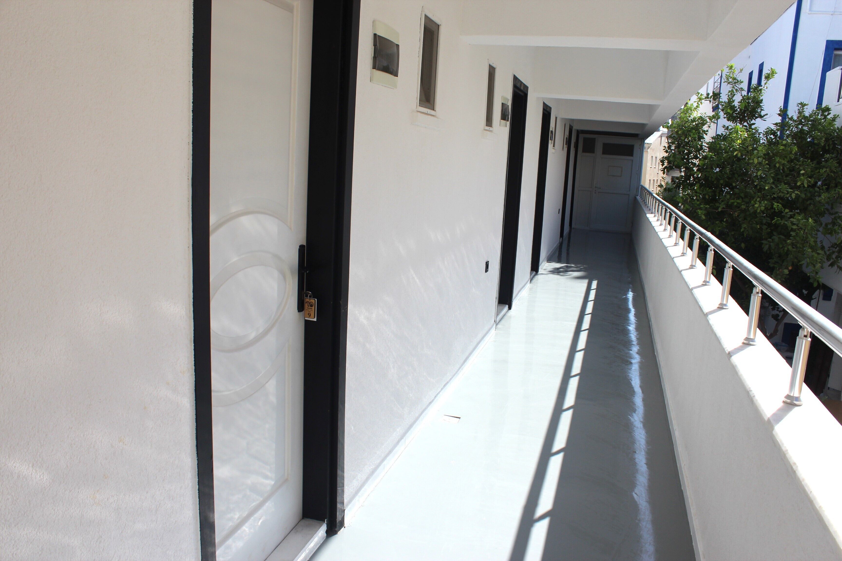A narrow corridor with white walls and black doors, leading to a balcony with a metal railing.