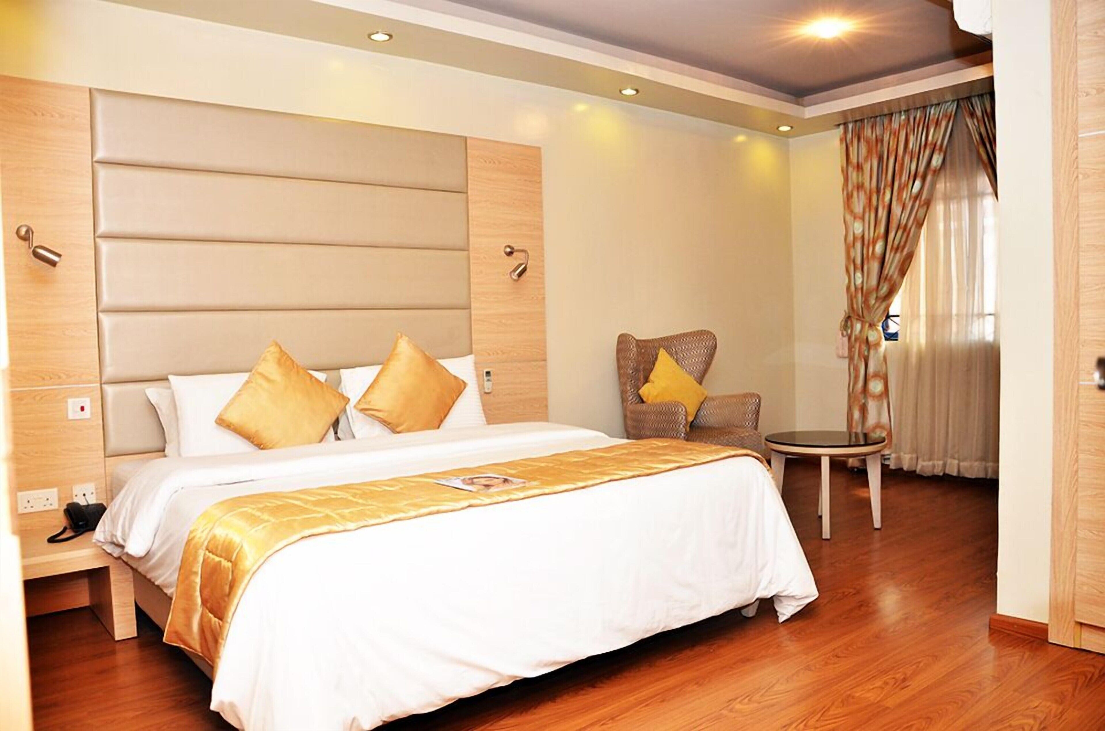 A hotel room with a large bed, a small round table, a chair, and a wardrobe.