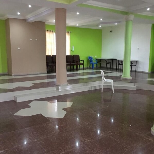 Um hall amplo com piso de mármore, paredes verdes e bege, e área de estar com cadeiras e mesas.