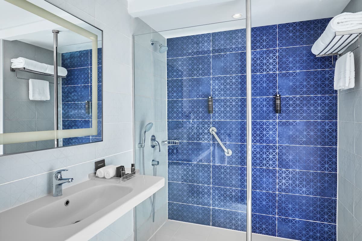 A modern bathroom with a glass shower enclosure, a white sink, and a large mirror.