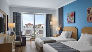 Habitación de hotel con dos camas, un escritorio, un televisor y un balcón con vistas a edificios.
