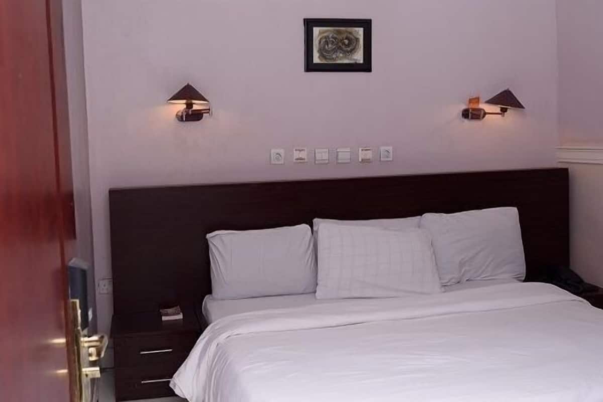 A hotel room with a large bed, two bedside lamps, a framed artwork above the bed, and a nightstand with a phone.