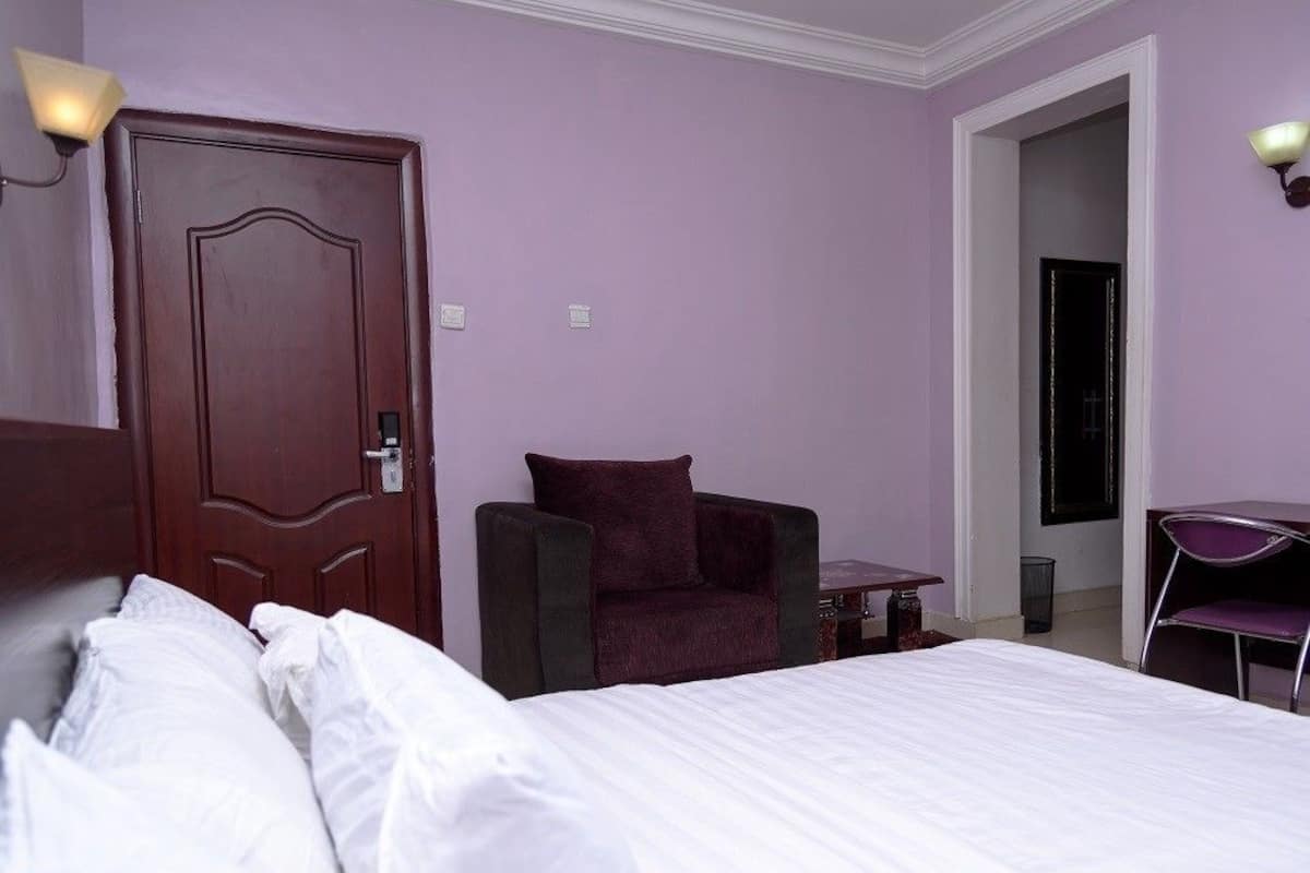 A hotel room with a large bed, a chair, a small table, and a door.