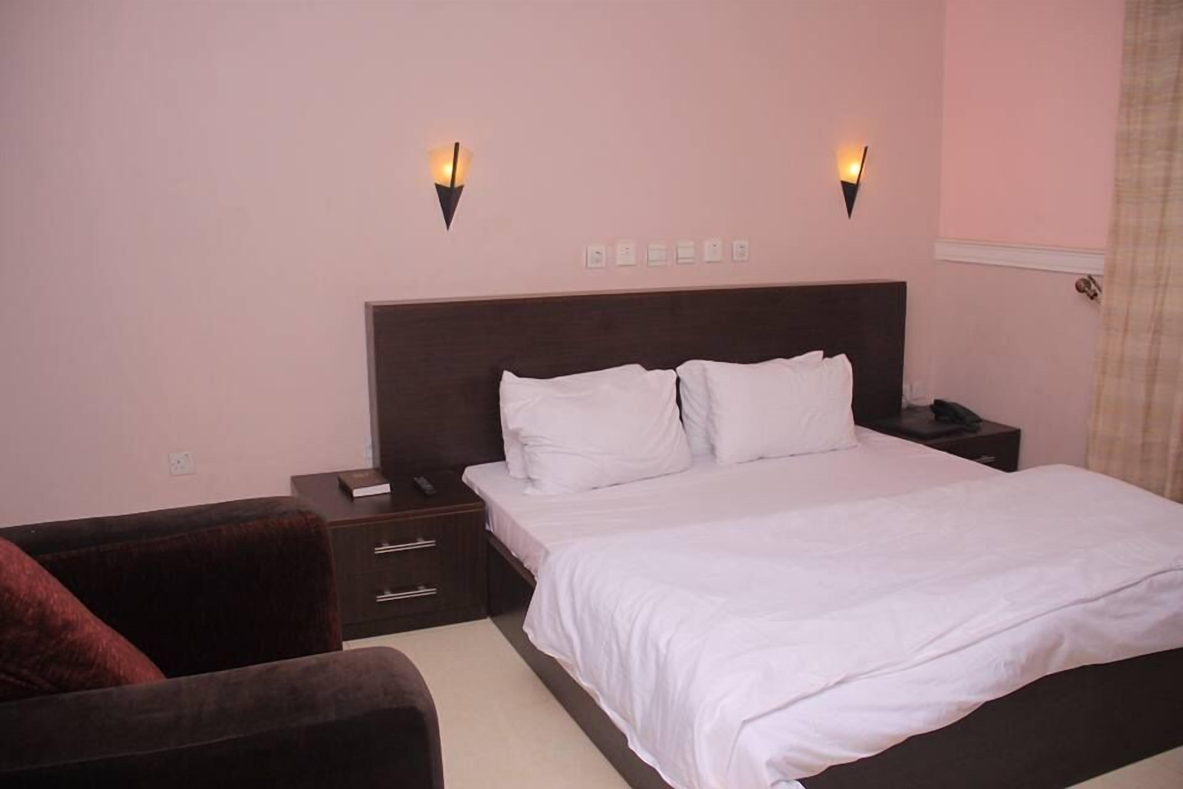 A bedroom with a large bed, two bedside tables, a nightstand, a chair, and two wall-mounted lights.