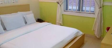 A hotel room with a bed, a nightstand, a lamp, and a window with curtains.