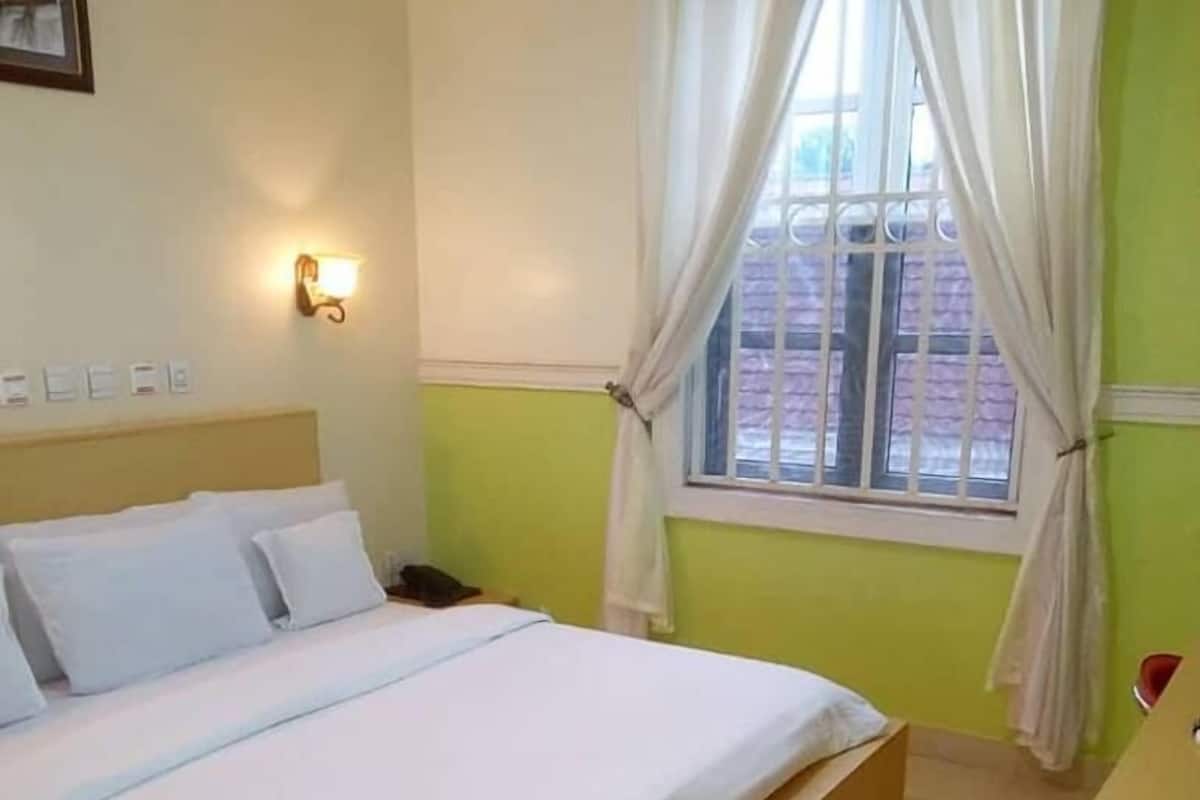 A hotel room with a bed, a bedside table, a lamp, and a window with curtains.