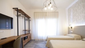 Habitación de hotel con un escritorio de madera, televisión, dos camas y un gran ventanal con cortinas.
