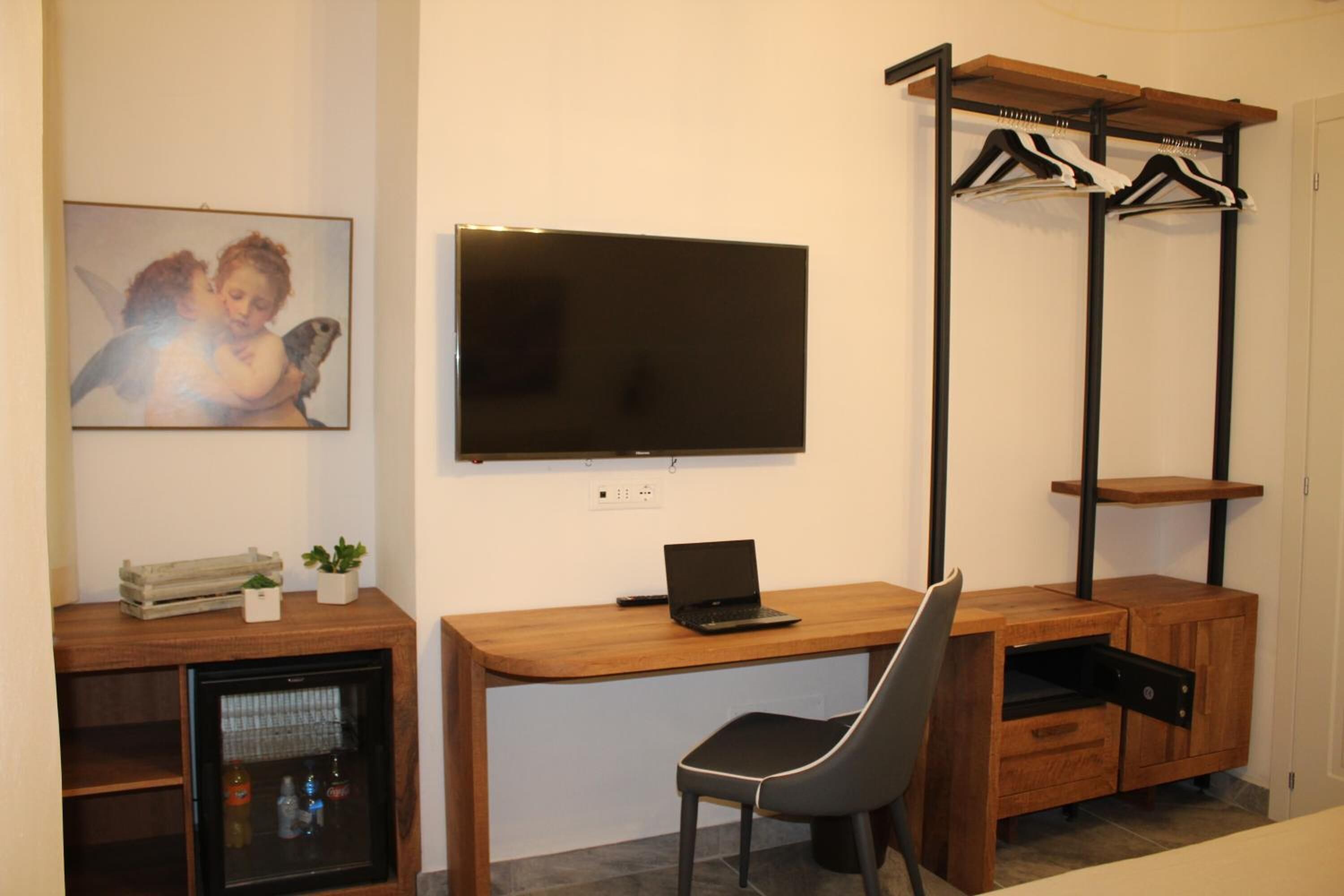 Une pièce de taille modeste, comprenant un bureau en bois, une chaise, un téléviseur fixé au mur et un petit réfrigérateur.