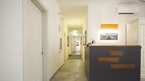 Zona de recepción de hotel, con mostrador de recepción, pasillo que lleva a las habitaciones y una escalera.