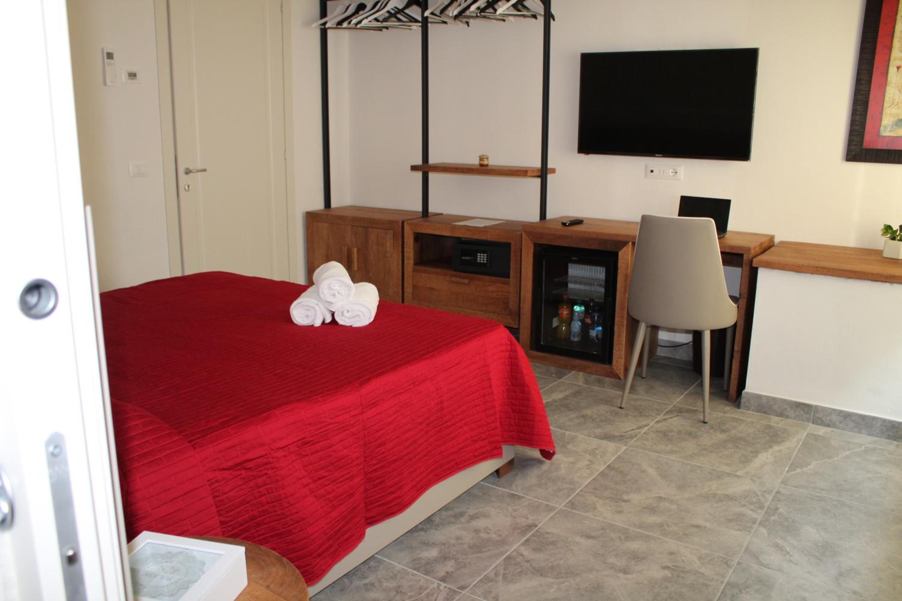 A hotel room with a bed, a desk, a chair, a TV, and a minibar.
