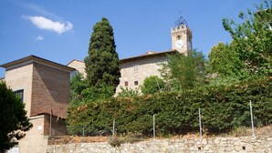 Un edificio histórico con una torre del reloj, rodeado de árboles y un muro de piedra.