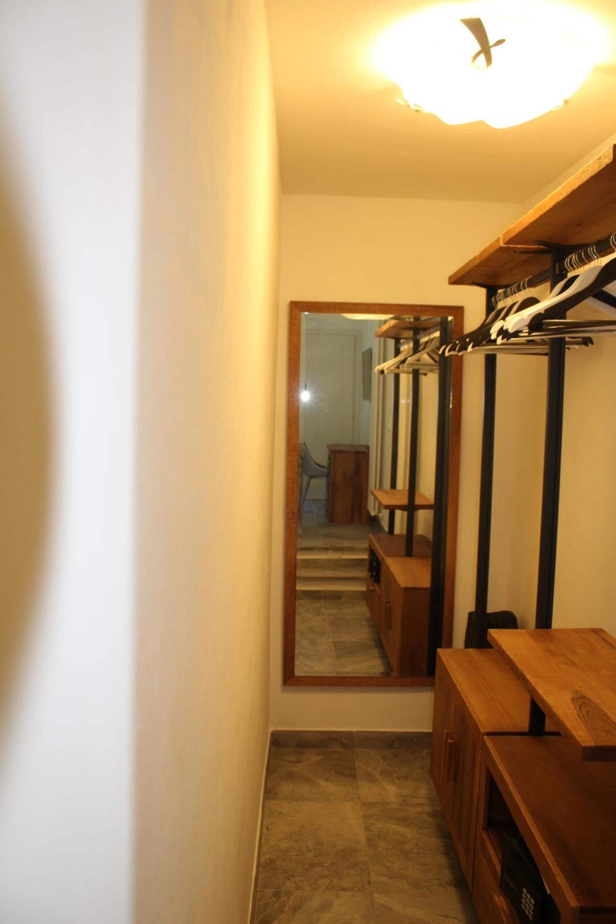 A narrow hallway with a wooden bench, a coat rack, and a mirror reflecting a staircase.