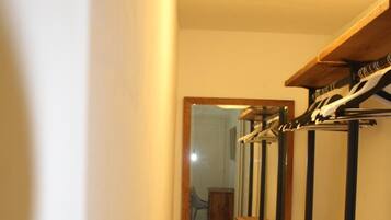 A narrow hallway with a wooden bench, a coat rack, and a mirror reflecting a staircase.