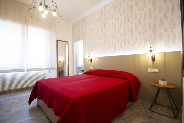 A hotel room with a large bed, a small table with a plant, and a mirror on the wall.