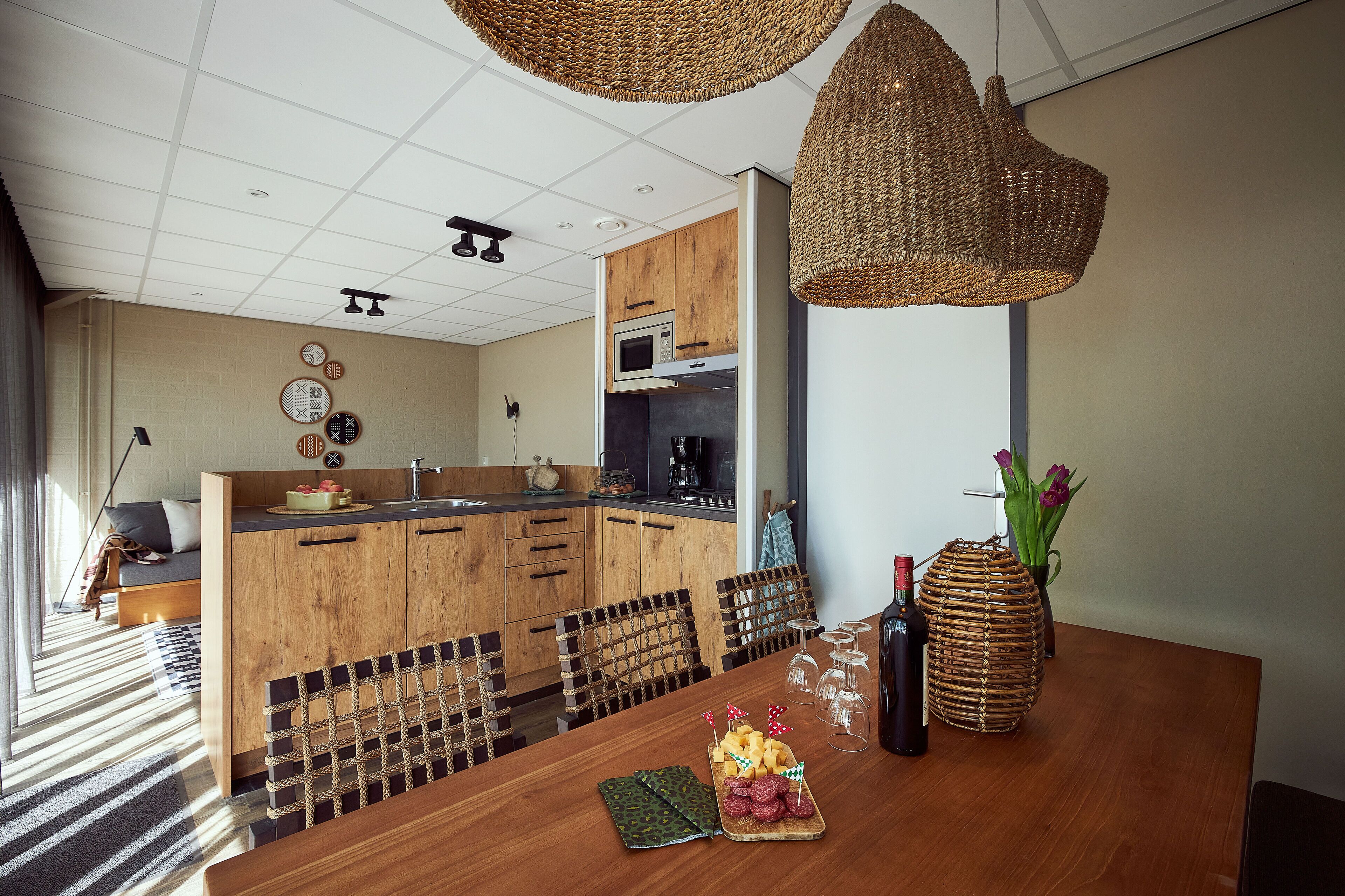 Una cocina moderna con armarios de madera, microondas integrado y zona de comedor con una mesa de madera lista para una comida.