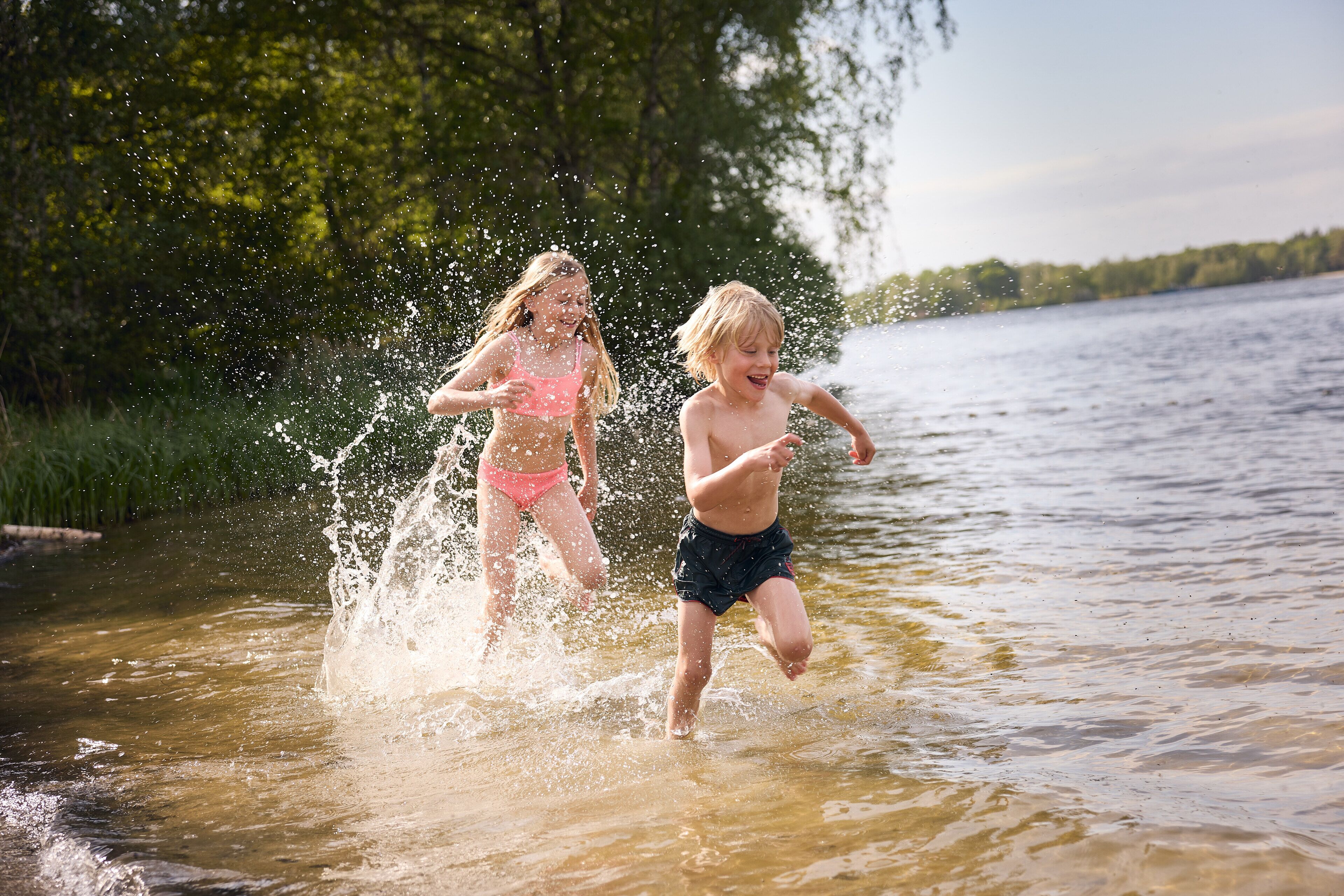 Two children playing in a shallow body of water surrounded by greenery.