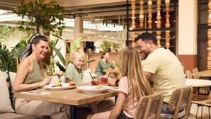 A family dining at a restaurant with wooden tables and chairs, surrounded by indoor plants and a modern interior design. - Lake Resort Beekse Bergen (Hilvarenbeek)