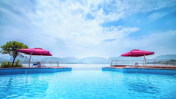 A swimming pool with two pink umbrellas and lounge chairs, surrounded by mountains and a clear sky. - Wingtech Hotel (Huangshi)