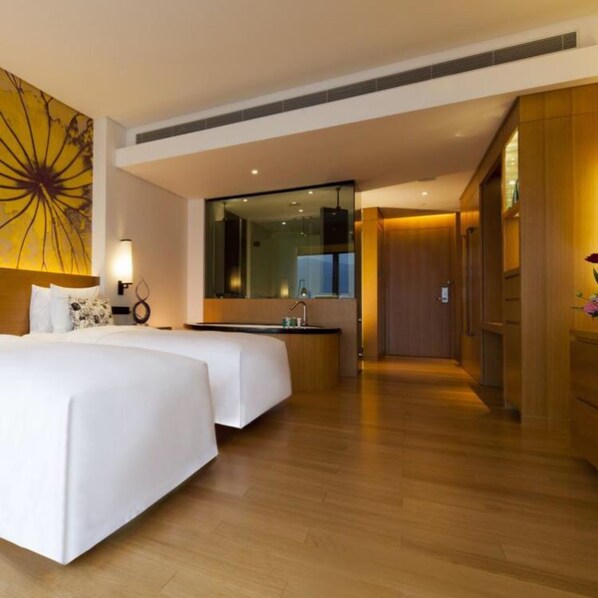 A hotel room with two beds, a large mirror, a sink, and a wooden floor.