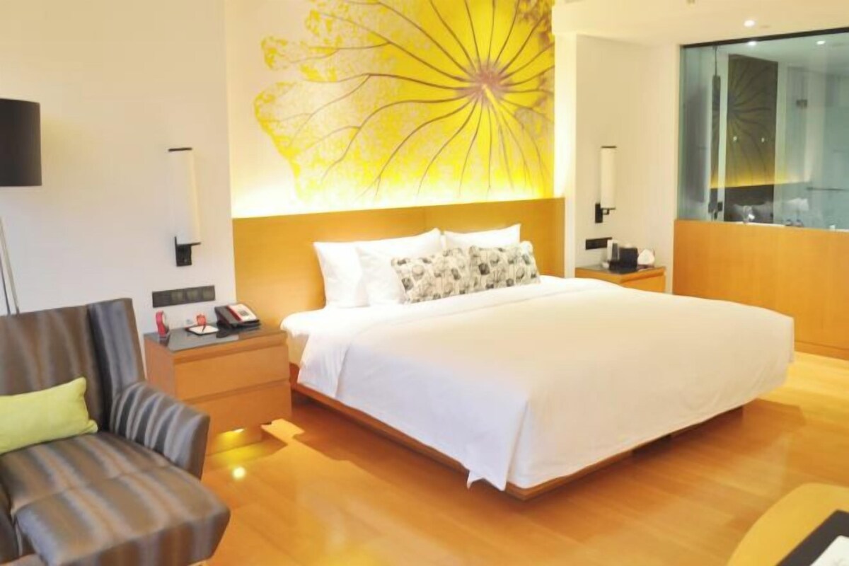 A hotel room with a large bed, a desk with a lamp, a chair, and a wall with a yellow floral design.